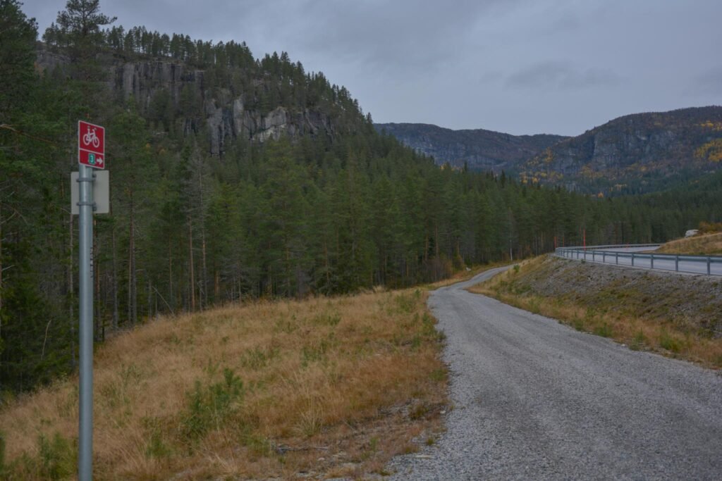 Når du har passert den lange svingen med den svære fjellskjeringa på "nye" Riksveg 9 nord for Bjørnarå, ser du straks den gamle Postvegen som ein fin, oppgrusa turveg på nedsida (vestsida) av vegen. Foto.