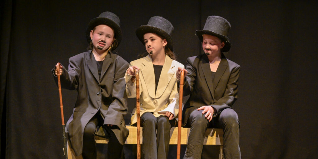 De tre late herremenn sittende på benken. Foto.